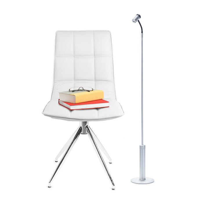 Cordless LightBob LED Task Light with adjustable neck, standing next to a contemporary white chair with books, for focused illumination.