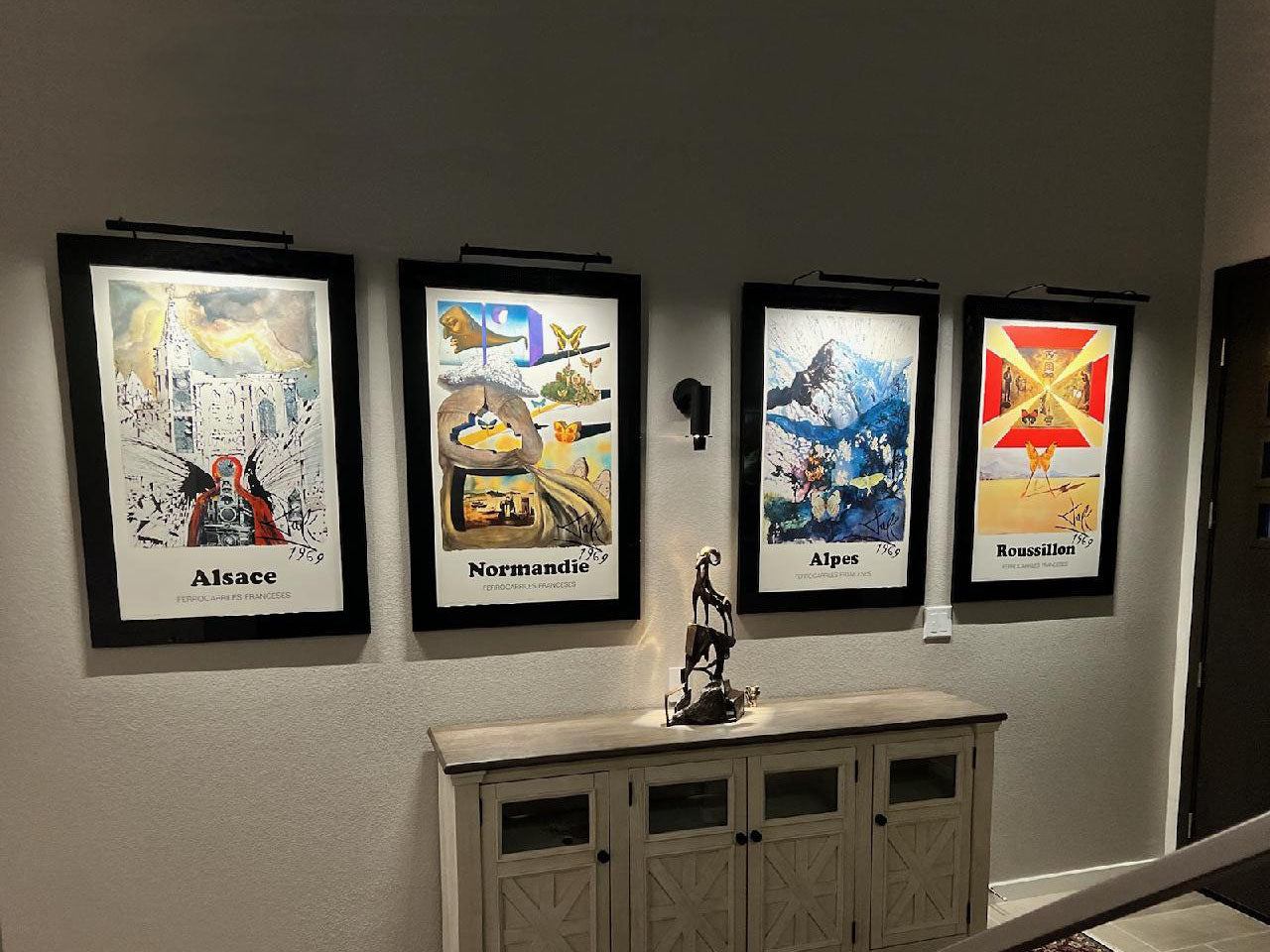 Four framed art prints illuminated by sleek art lights, enhancing the vibrant colors and details of each piece