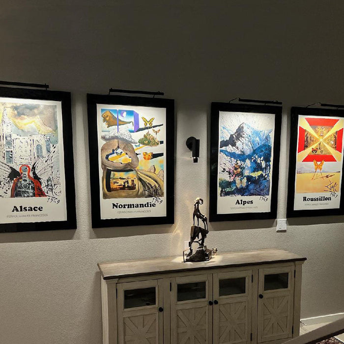 Four framed art prints illuminated by sleek art lights, enhancing the vibrant colors and details of each piece