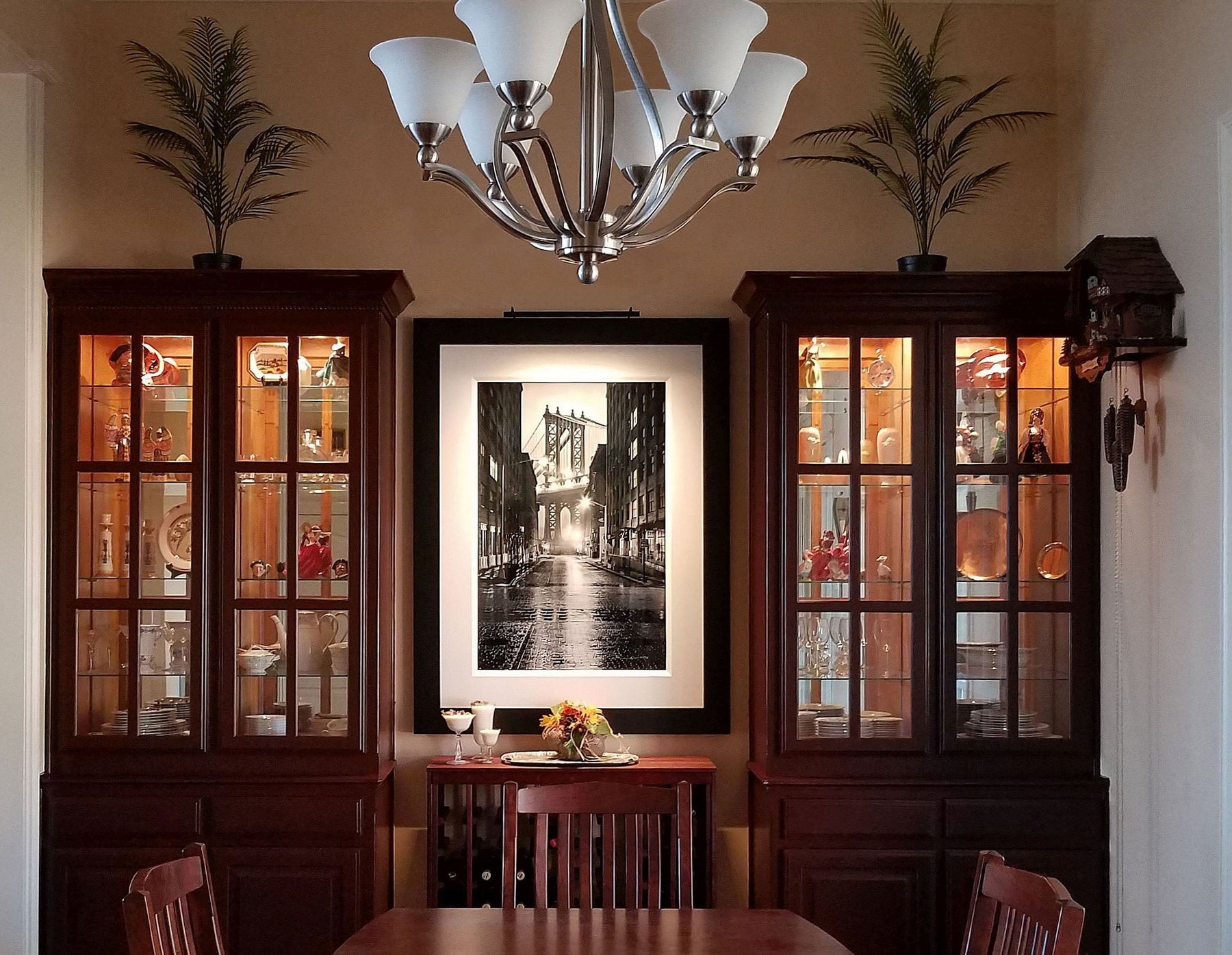 Black-and-white framed artwork illuminated by a Plug-in Vision Series art light in an elegant dining room with dark wood cabinets and decor.