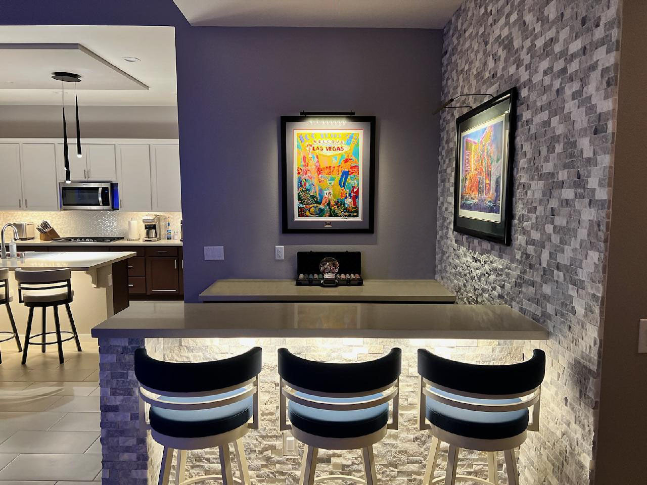 Modern kitchen bar area highlighted by well-lit vibrant artwork with specialized art lighting fixtures enhancing visual appeal.