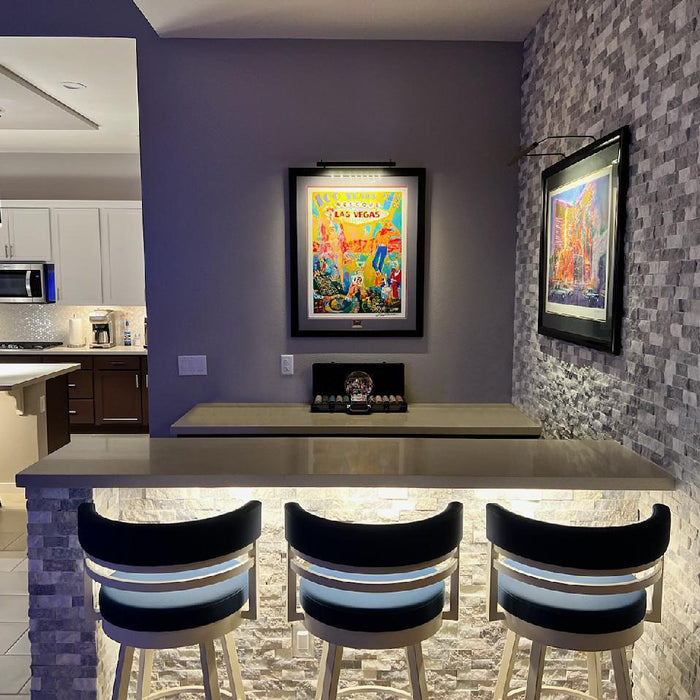 Modern kitchen bar area highlighted by well-lit vibrant artwork with specialized art lighting fixtures enhancing visual appeal.
