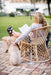 Woman reading outdoors comfortably seated in a wicker chair, using the portable LightBob™: a cordless, go-anywhere LED task floor light, providing focused illumination on her book.